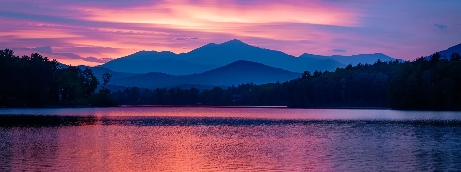 a vibrant sunset casts radiant hues of orange and pink over a tranquil lake, illuminating the silhouette of a majestic mountain range in the distance.